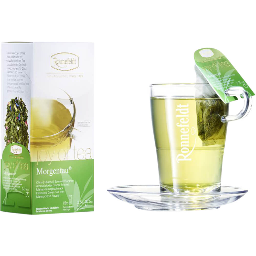 Ronnefeldt Joy of Tea Morgentau® als Serviervorschlag: Glas mit aufgebrühtem Tee, Teebeutel am Rand, und Packung im Hintergrund – frischer, exotisch-fruchtiger Grüntee