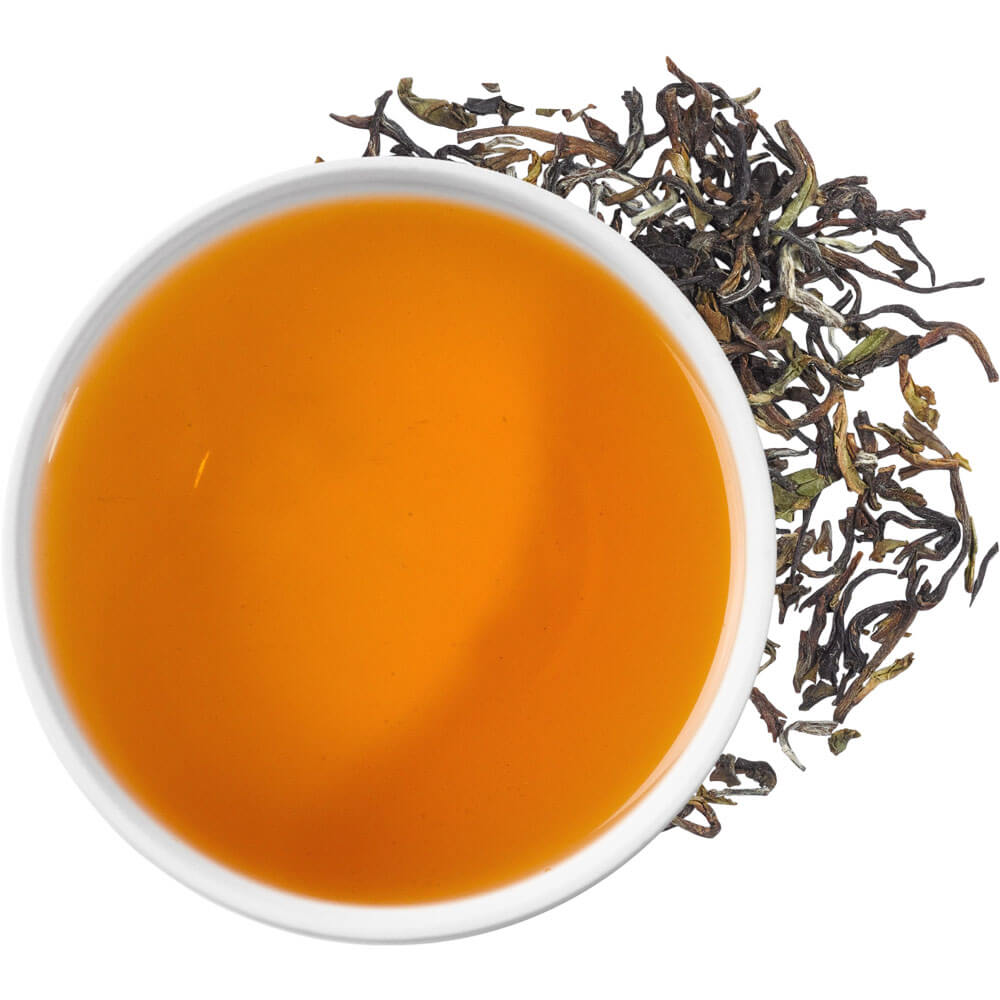 Tasse mit bernsteinfarbenem Aufguss des Sikkim Temi First Flush Bio-Schwarztees und trockene Teeblätter daneben